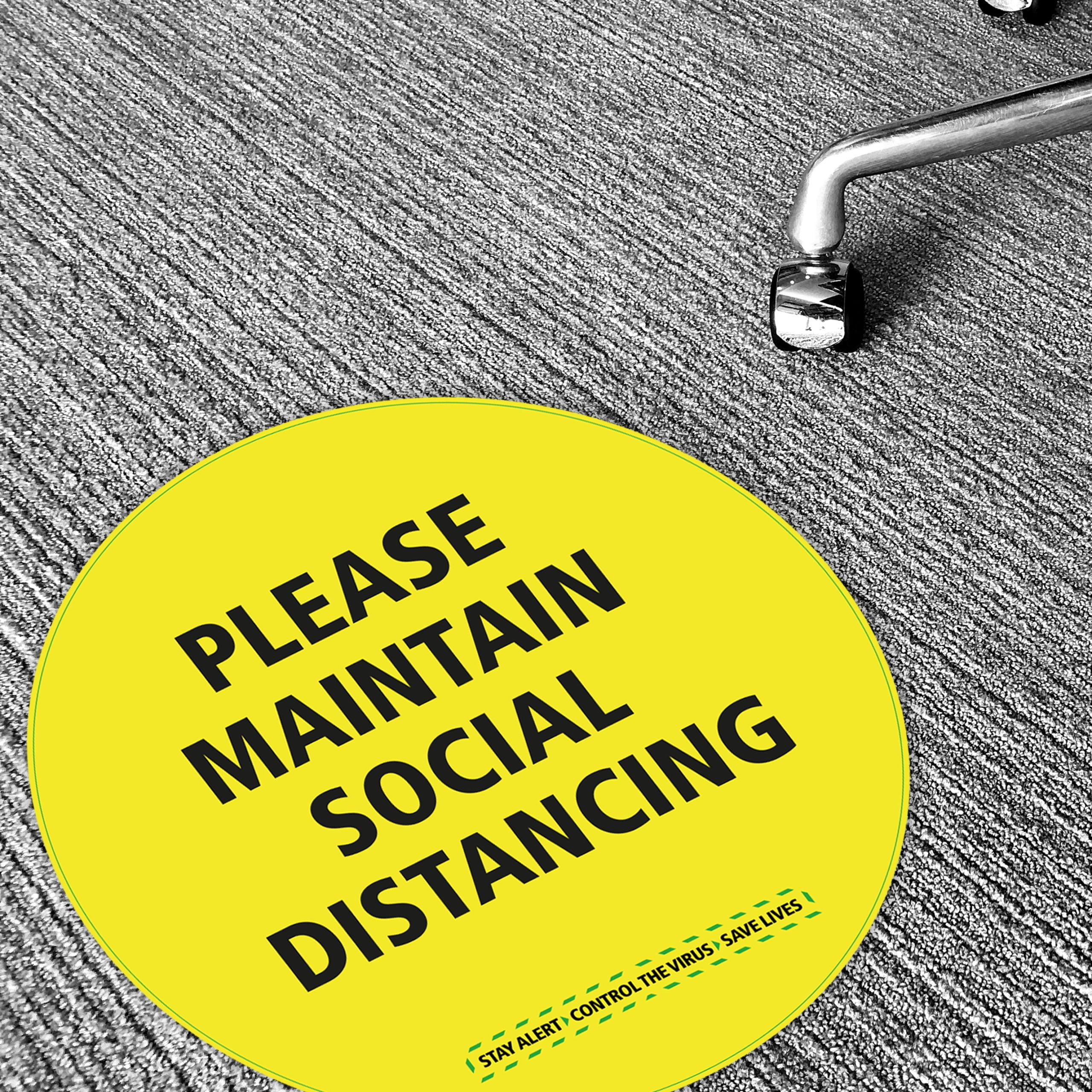 Indoor Carpet (R10)- 115 | Yellow circular floor sticker reading “Please Maintain Social Distancing” applied to grey short pile carpet with castor chair in view