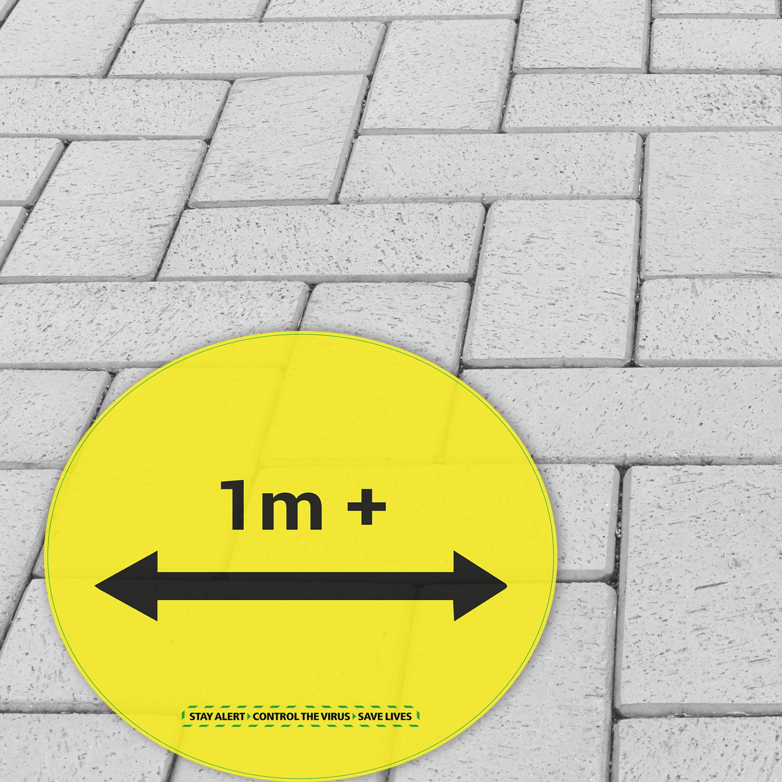 Yellow circular floor sticker with “1m+” distancing message applied to outdoor block paving surface printed on R9 anti-slip vinyl