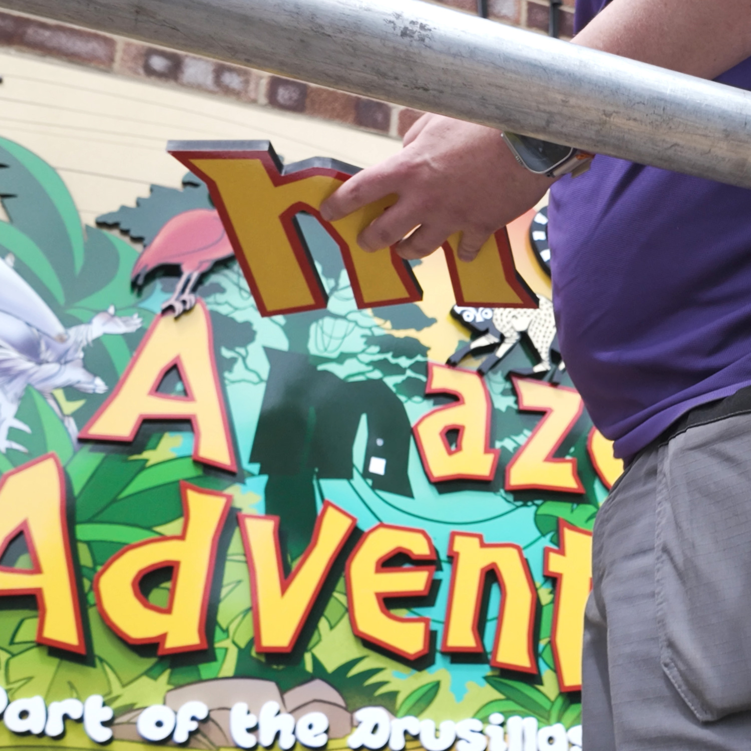 Installer positioning a letter during the final assembly of the colourful “Amazon Adventure” sign at Drusillas Park.