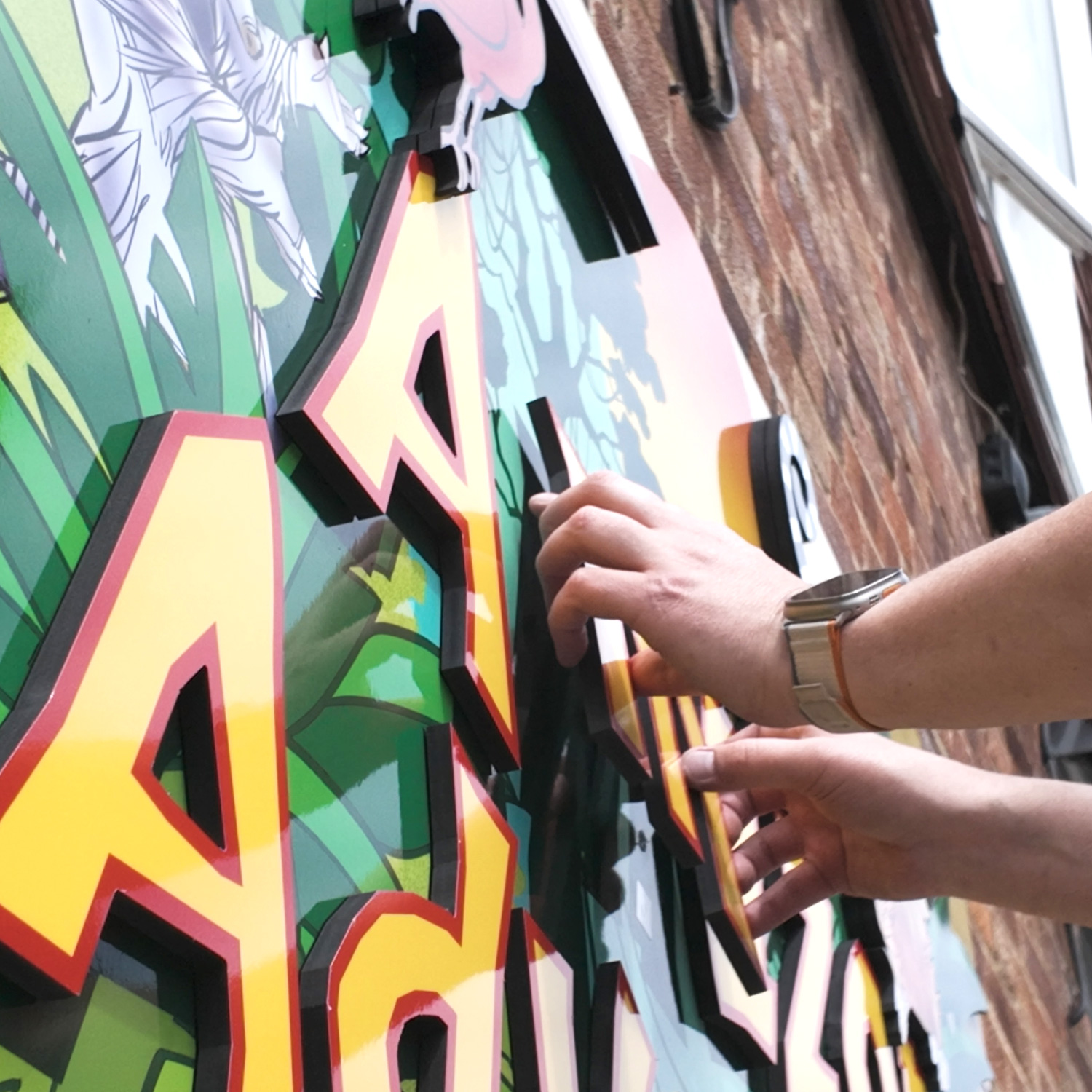 Technician installing the 3D “Amazon Adventure” sign at Drusillas Park, securing layered graphics to the wall.