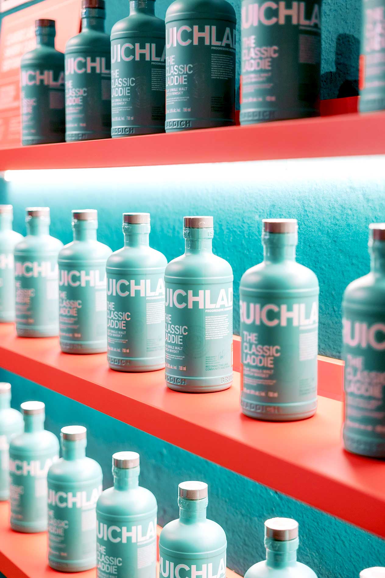 Close-up of Bruichladdich The Classic Laddie bottles on red shelf against turquoise wall, produced for Rémy Cointreau exhibition by Beautiful LFP.